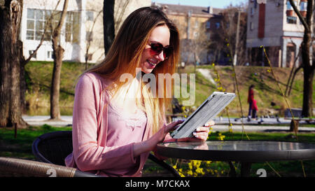 Gladden girl faisant appel vidéo en un comprimé à l'petit ami dans un parc Banque D'Images