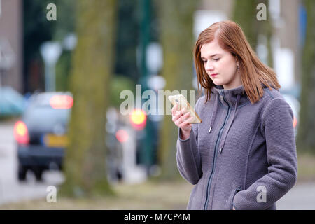 Jeune femme vérifié son téléphone cellulaire pour les nouveaux messages à l'extérieur Banque D'Images