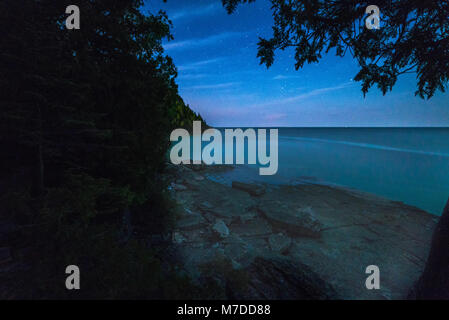 Voie lactée et ciel étoilé avec nuages vaporeux le long des rives de la baie Georgienne dans la nuit avec la silhouette des arbres et rochers dans l'eau claire Banque D'Images