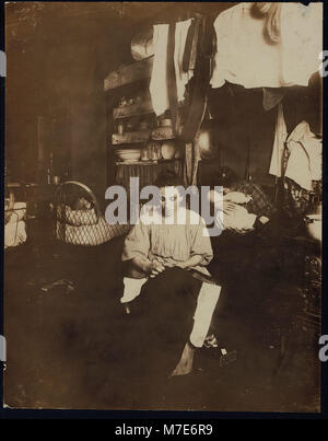 Cette image montre MRS Tony Racioppo travaillant sur la finition de pantalons dans un immeuble délabré au 260 Elizabeth Street, New York. La maison, bien que autorisée, est en mauvais état, reflétant les conditions de vie de l'époque. Banque D'Images