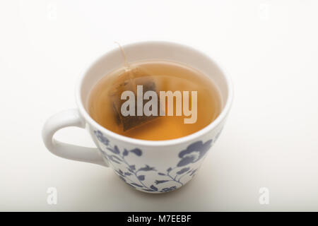 Sachet de trempage dans l'eau bouillante dans un verre pendant la préparation d'une tasse de thé sur un fond blanc Banque D'Images