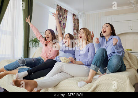 Les jeunes filles de regarder la télévision, eating popcorn assis sur le canapé. Banque D'Images