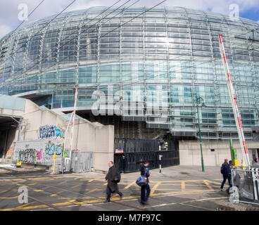 DUBLIN, IRLANDE - 6 mars 2018 : Les personnes qui franchissent la ligne de tramway et la route. Dans l'arrière-plan est l'Aviva Stadium. Banque D'Images