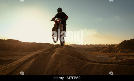 Pilote Moto Motocross professionnel de la conduite sur la dune et plus loin sur la piste tout terrain. C'est le coucher du soleil et la voie est recouverte de brouillard de fumée/. Banque D'Images