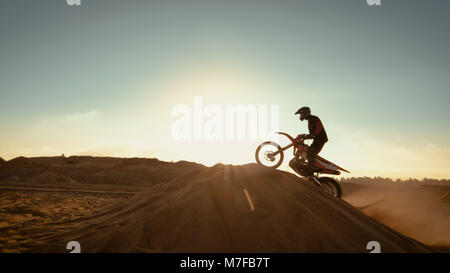 Pilote Moto Motocross professionnel saute au-dessus de la dune et plus loin sur la piste tout terrain. Tourné sur une carrière abandonnée alors que soleil se couche. Banque D'Images