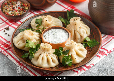 - Khinkali boulettes géorgiennes avec de la viande et le persil dans un plat de céramique avec une sauce de crème sure et de verts. Selective focus Banque D'Images