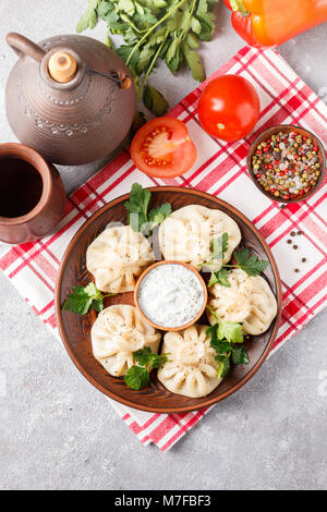 - Khinkali boulettes géorgiennes avec de la viande et le persil dans un plat de céramique avec une sauce de crème sure et de verts. Focus sélectif. Vue d'en haut Banque D'Images