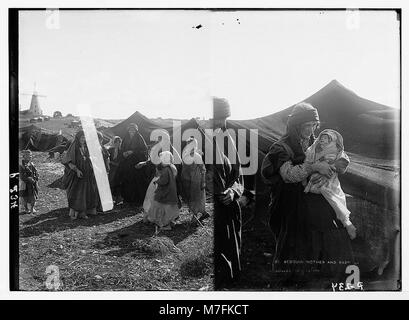 Photographie de femmes et d'enfants bédouins devant une tente, avec un moulin à vent en arrière-plan. L'image montre une mère tenant un bébé emmailloté, reflétant la vie bédouine traditionnelle en TRANS-Jordanie. Banque D'Images