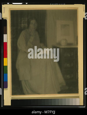 Beatrice Baxter Ruyl, une femme habillée en tenue formelle, assise avec un livre ouvert sur ses genoux et la main sur son visage, capturée dans un moment calme et introspectif. Banque D'Images