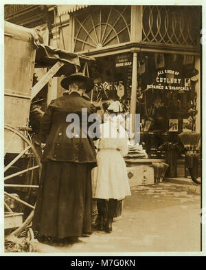 Portrait d'un jeune vendeur, probablement capturé dans un cadre de marché de rue. Cette image offre un aperçu de la vie quotidienne d’un jeune entrepreneur au début du XXe siècle. Banque D'Images