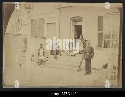 Une photographie montrant deux soldats non identifiés et d'autres debout sur les marches avant d'une maison, capturant un moment de la vie quotidienne au début du XXe siècle. Banque D'Images