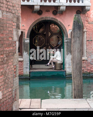 Fille assise sous une arche près d'un canal avec un bouquet de roses à la main, Venise, Italie Banque D'Images