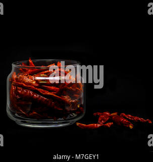 Piments rouges séchés dans des contenants de verre à fond noir Banque D'Images