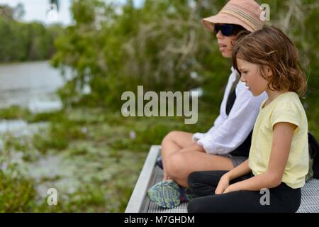 Mère et fille s'asseoir sur le quai donnant sur l'eau et la forêt tout en discutant, Apex Park Drive, Condon Riverway, QLD, Australie Banque D'Images