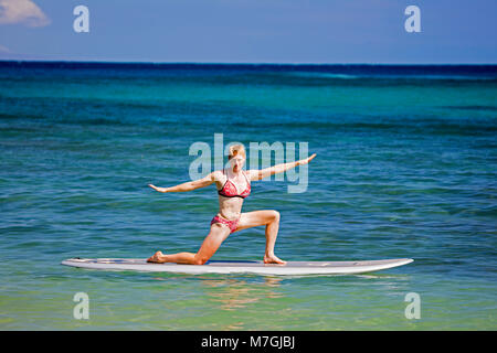 Une femme sur un stand-up paddle board dans une position de yoga, Maui, Hawaii. Banque D'Images