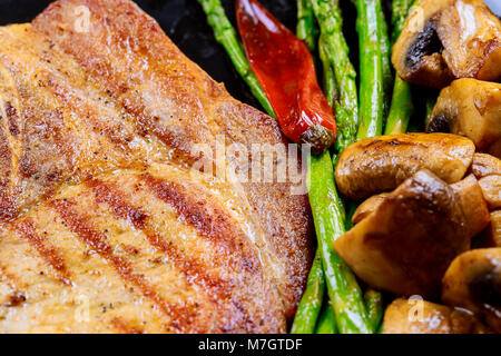 Steaks de porc aux herbes, asperges, champignons fry sur fond ardoise close up. Plats de viande chaude Banque D'Images