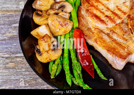 Faux filet grillé steak en tranches. Épais juteux steak grillé assaisonné avec les asperges et les champignons frais de l'été, barbecue. Des légumes sur une plaque noire w Banque D'Images