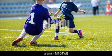 Jeune gardien de football enregistrer. Garçon attraper un ballon de football. Banc et l'équipe de football des enfants à l'arrière-plan. Match de football pour les enfants Banque D'Images