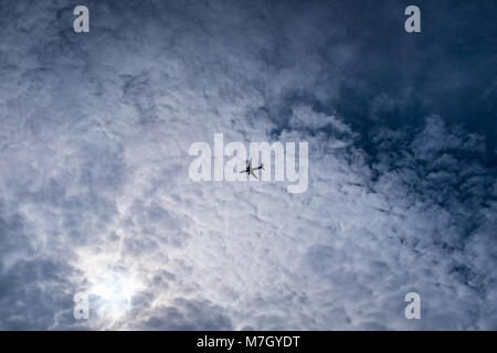 En silhouette avion voler à travers les nuages cirrocumulus texturé vu depuis le sol Banque D'Images