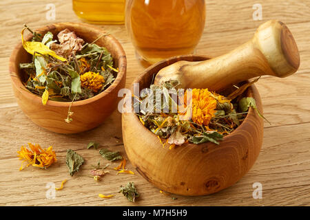 Belle la vie toujours de deux pots d'huile en verre transparent, avec mortier et pilon en bois motley colorés de l'herbe, y compris coltsfoot, tilleul et calendula Banque D'Images