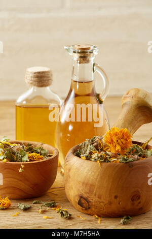 Belle la vie toujours de deux pots d'huile en verre transparent, avec mortier et pilon en bois motley colorés de l'herbe, y compris coltsfoot, tilleul et calendula Banque D'Images