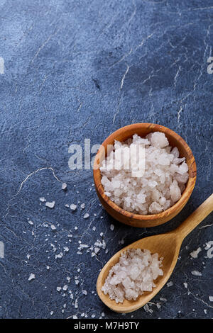 Large White les cristaux de sel de mer dans un bol en bois naturel et la cuillère pleine de sel sur fond sombre, vue du dessus, close-up, selective focus, faible profondeur o Banque D'Images