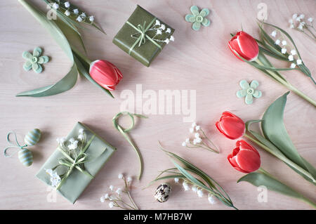 Vue de dessus de table en bois clair avec des décorations printanières, les cadeaux emballés, fleurs blanches, tulipes rouges et et les oeufs de Pâques. Printemps ou Pâques zone Banque D'Images