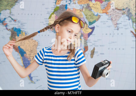 Pretty Little girl holding vintage camera et ses tresses sur fond de carte du monde Banque D'Images