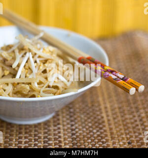 Nouilles de riz coréen avec les germes de soja et les arachides broyées dans le bol blanc avec des baguettes Banque D'Images