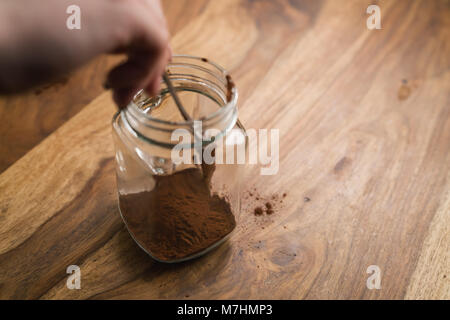 Faire de boisson au cacao dans un bocal en verre avec poignée en bois sur le tableau, l'ajout de cacao poudre, focus peu profondes Banque D'Images