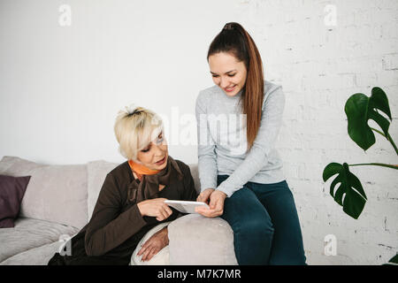 Une jeune fille explique à une femme âgée comment utiliser une tablette ou manifeste une certaine application ou vous enseigne comment utiliser un réseau social. L'enseignement de l'ancienne génération des nouvelles technologies. Banque D'Images