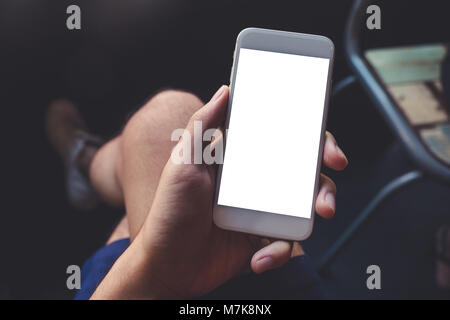 Image d'une maquette man's hand holding white téléphone mobile avec écran de bureau en blanc sur la cuisse avec des chaussures en toile blanche, café avec détendre Banque D'Images