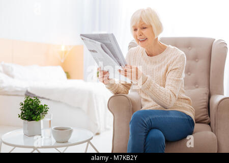 Happy senior femme lisant un article merveilleux dans un journal et souriant Banque D'Images
