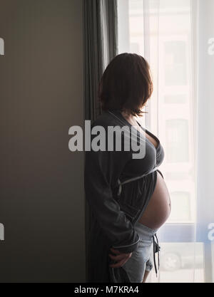 Une femme enceinte regarder par la fenêtre. Banque D'Images