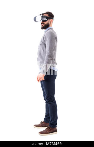 Vue latérale du smart casual man barbu gilet gris regardant vr lunettes. Corps plein isolé sur fond blanc. Banque D'Images