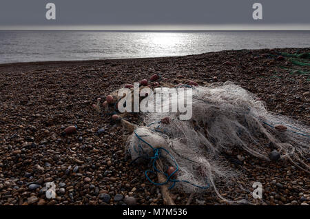 Filet de pêche en nylon dans un tas sur une plage de galets avec la mer en arrière-plan et la lumière diffusée sur le net scintillants Banque D'Images