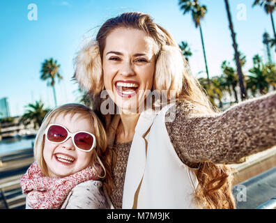 À Barcelone pour un hiver parfait. smiling young mother and daughter touristes sur le quai à Barcelone, Espagne prendre des selfies Banque D'Images