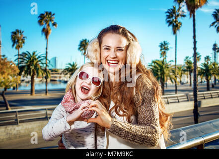 À Barcelone pour un hiver parfait. Portrait de la mère et de l'enfant moderne heureux touristes sur le quai à Barcelone, Espagne montrant les mains en forme de coeur Banque D'Images