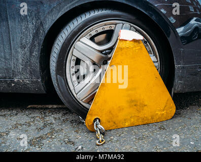 Triangle jaune collier roue fermée avec messing lock et la chaîne sur une voiture en stationnement illégal Banque D'Images