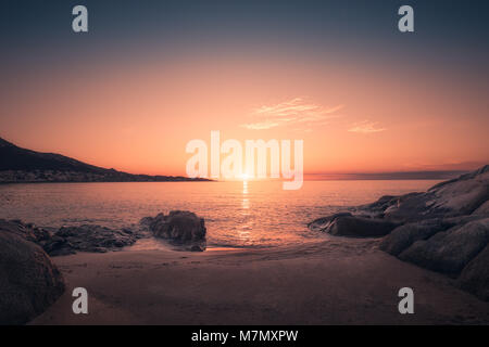 Coucher de soleil sur les affleurements rocheux et petite plage de sable à Algajola en Balagne Corse Banque D'Images