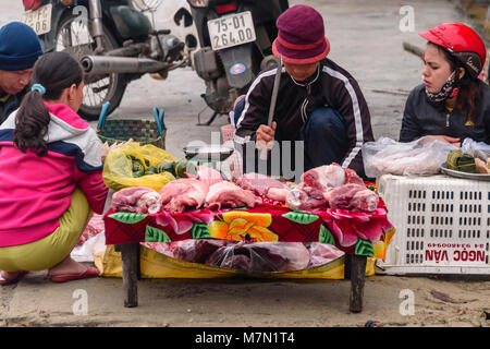 Une femme coupe la viande dans son magasin à bouchers Hue, Vietnam. La boutique est sur le trottoir par une route, et la viande est assis sur une feuille de plastique sur une petite table en bois. Elle utilise une dalle de béton comme une planche. Banque D'Images