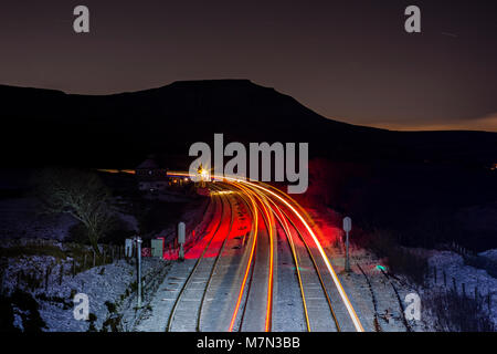 Northern rail du passage des trains dans la nuit noire à Blea Moor (au nord de Ribblehead) avec la neige au sol, Ingleborough se profile derrière Banque D'Images