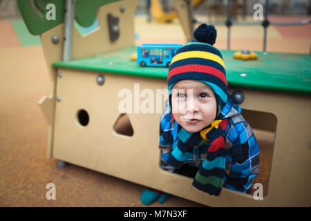 Bel enfant est assis en petite maison à l'aire de jeux. Petit garçon pensif rêve et sourit mystérieusement dans la cour Banque D'Images