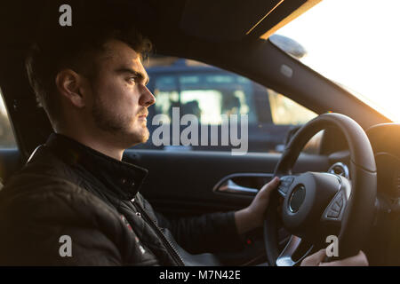 Jeune homme concentré au volant la voiture de luxe. Guy grave à l'avant et tient les mains sur la roue. Un homme qui avait réussi à se dépêcher pour affaires. Vue de côté Banque D'Images