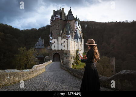 Belle jeune femme avec bouteille de vin se trouve sur la route menant à un château incroyable. Lieu médiéval fantastique. Les rayons de soleil tombent sur les cheveux Banque D'Images