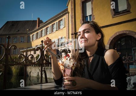 Jeune femme assise dans un café local à city promenade en Alsace et détient le verre avec de la glace. Trendy girl mange de dessert sur la terrasse au lieu romantique Banque D'Images