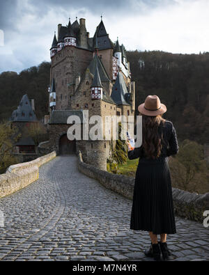 Jeune femme avec bouteille de vin se trouve sur la route menant à château fabuleux. La place médiévale incroyable. Trendy girl est voyager en Europe Banque D'Images