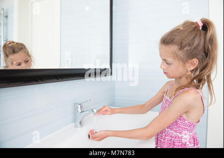 Petite fille en robe se lave les mains dans le lavabo dans la salle de bains Banque D'Images