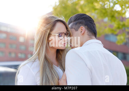 Jeune femme blonde chuchote à l'homme l'amour à l'extérieur en ville, déclaration d'amour Banque D'Images