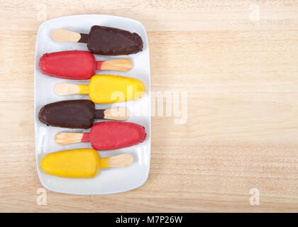 Bonbons colorés couverts sucettes gâteau sur une assiette blanche alternant saveurs et direction de cake pops, étendu sur une table en bois clair. Fun anniversaire partie Banque D'Images